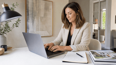 A real estate agent typing a property listing description on a laptop with handwritten notes nearby