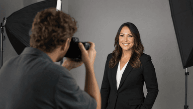 A professional photographer taking a headshot portrait of a real estate agent against a plain studio backdrop