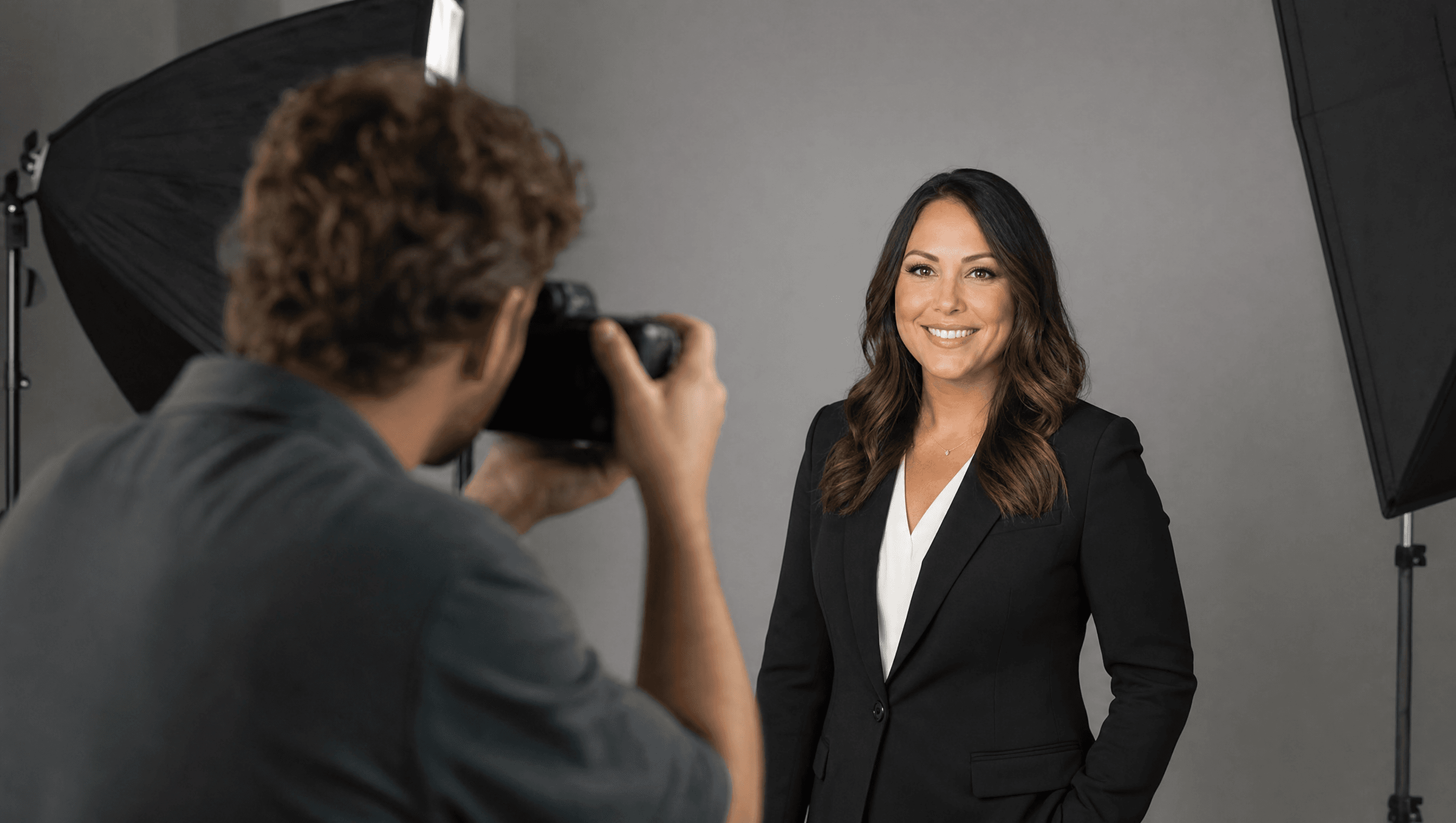 A professional photographer taking a headshot portrait of a real estate agent against a plain studio backdrop